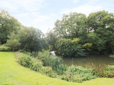 A pond surrounded by grass and trees at 6 Streamside in Lanreath