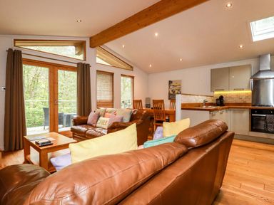 A living room with brown leather sofas a wooden coffee table a dining table and a kitchen area at 6 Streamside in Lanreath