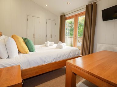A bedroom with a bed with yellow and green pillows white towels on the bed wooden furniture and a wall mounted tv at 6 Streamside in Lanreath