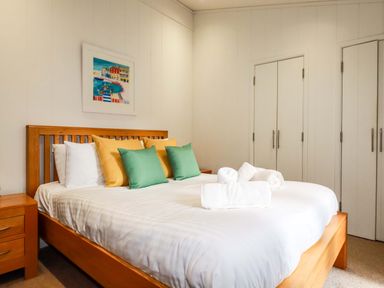 A bedroom with a wooden bed and two nightstands with cushions and rolled towels on the bed at 6 Streamside in Lanreath