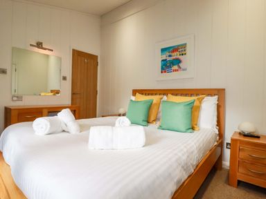 A bedroom with a wooden bed and side tables with green and yellow cushions and rolled white towels on the bed at 6 Streamside in Lanreath