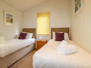 A bedroom with two single beds a window with blinds and a nightstand at 6 Streamside in Lanreath