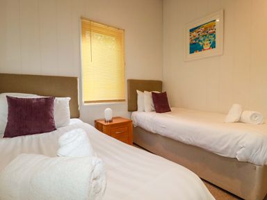 A bedroom with two single beds bedside table lamp window blinds and framed artwork at 6 Streamside in Lanreath
