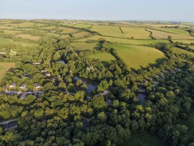 An aerial view of fields, trees, and houses near a pond at 6 Streamside in Lanreath