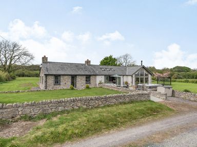 A stone cottage with a slate roof and a fenced garden in a rural setting at Hen Hafod in Talwrn near Llangefni