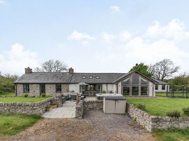A stone and white exterior house with a paved patio outdoor furniture and grass at Hen Hafod in Talwrn near Llangefni
