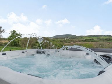 A jacuzzi with water jets in an outdoor setting with fields and hills in the background at Hen Hafod in Talwrn near Llangefni