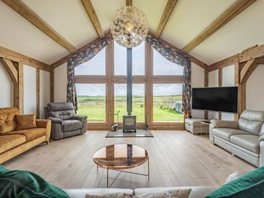 A living room with sofas a wood stove a large window and a wall mounted television at Hen Hafod in Talwrn near Llangefni