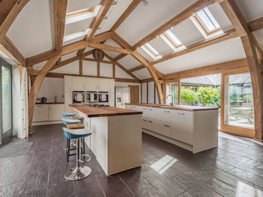A kitchen with wooden beams white cabinets kitchen islands stools and skylights at Hen Hafod in Talwrn near Llangefni
