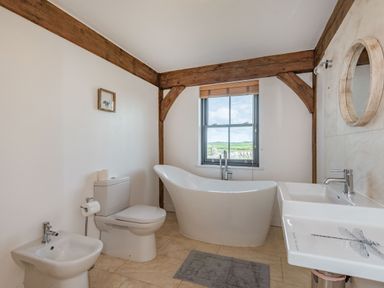 A bathroom with a bathtub near a window a toilet a bidet a sink and wooden ceiling beams at Hen Hafod in Talwrn near Llangefni