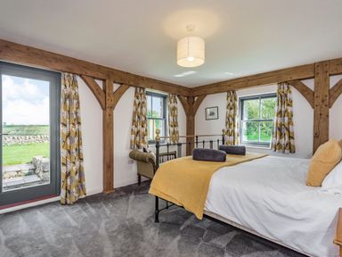 A bedroom with a bed a small sofa patterned yellow curtains and exposed wooden beams at Hen Hafod in Talwrn near Llangefni