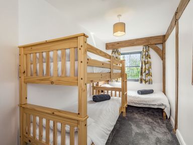 A bedroom with wooden bunk beds and a single bed with towels on white bedding at Hen Hafod in Talwrn near Llangefni
