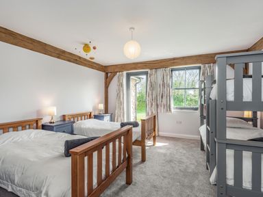 A bedroom with two single beds two bedside tables with lamps a bunk bed and windows with curtains at Hen Hafod in Talwrn near Llangefni