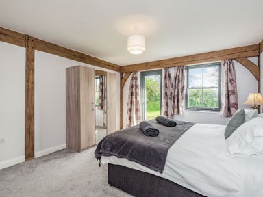 A bedroom with a double bed two rolled towels on a blanket a wardrobe and windows with floral curtains at Hen Hafod in Talwrn near Llangefni