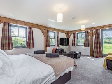 A bedroom with bed towels armchair ottoman television and windows at Hen Hafod in Talwrn near Llangefni