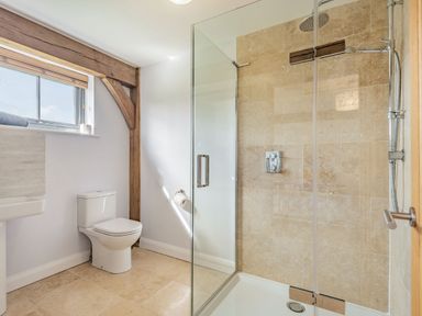 A bathroom with a toilet, a sink, and a glass-enclosed shower with beige tiles at Hen Hafod in Talwrn near Llangefni