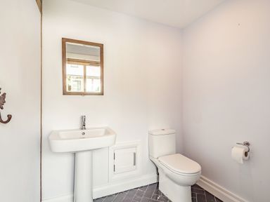 A bathroom with a sink pedestal mirror toilet and toilet paper holder at Hen Hafod in Talwrn near Llangefni