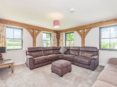 A living room with a sectional sofa and ottoman by windows with wooden beams at Hen Hafod in Talwrn near Llangefni