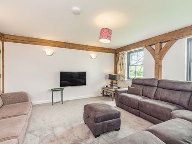 A living room with sofas ottoman a wall mounted television and wooden beams at Hen Hafod in Talwrn near Llangefni