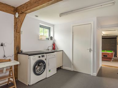 A laundry room with a washing machine, dryer, and sink with a window above at Hen Hafod in Talwrn near Llangefni