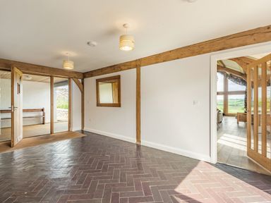 An empty hallway with dark herringbone floor a wooden framed mirror and open doors revealing a porch and a room with large windows at Hen Hafod in Talwrn near Llangefni