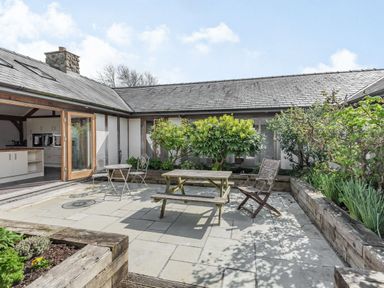An outdoor patio with wooden and metal chairs and tables surrounded by raised garden beds at Hen Hafod in Talwrn near Llangefni