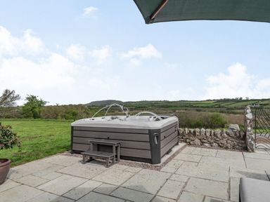 An outdoor hot tub with water jets on a stone patio overlooking fields and hills at Hen Hafod in Talwrn near Llangefni