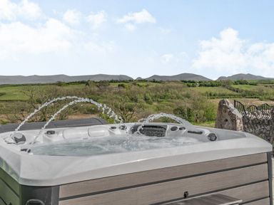 An outdoor hot tub with water jets and a view of green hills and trees at Hen Hafod in Talwrn near Llangefni
