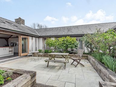 An outdoor patio with a wooden picnic table and chairs surrounded by raised garden beds at Hen Hafod in Talwrn near Llangefni