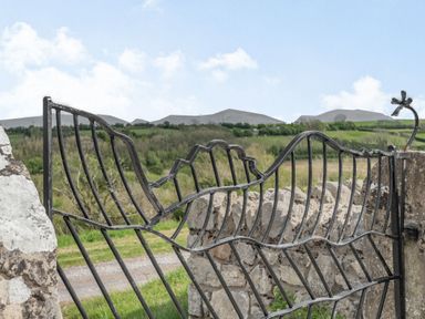 A metal gate with a flower design attached to a stone wall overlooking a rural landscape with hills at Hen Hafod in Talwrn near Llangefni
