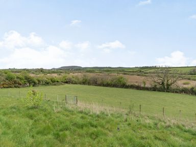 A fenced green field with a metal gate and trees in the background at Hen Hafod in Talwrn near Llangefni