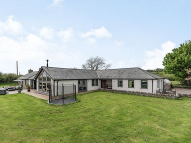 A large single story house with a grassy yard and a round trampoline at Hen Hafod in Talwrn near Llangefni