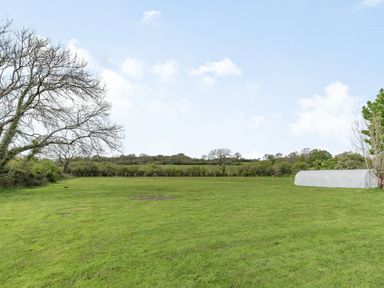 A large grassy field with a fenced boundary and trees at Hen Hafod in Talwrn near Llangefni