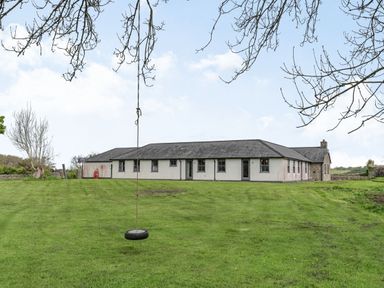 A house with multiple windows and doors on a grassy lawn with a tire swing hanging from a tree at Hen Hafod in Talwrn near Llangefni