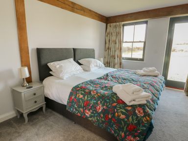 A bedroom with a double bed covered with floral bedspread and towels on top next to a window and a door at Hen Hafod in Talwrn near Llangefni