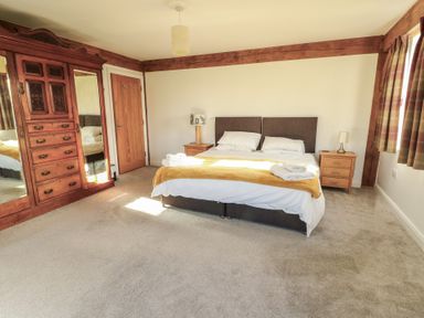 A bedroom with a double bed and wooden furniture including a wardrobe and bedside tables at Hen Hafod in Talwrn near Llangefni