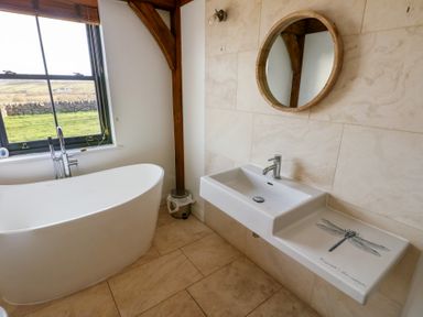 A bathroom with a freestanding bathtub next to a window and a sink with a dragonfly design on the countertop at Hen Hafod in Talwrn near Llangefni
