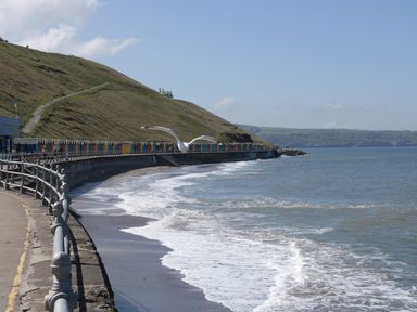 A coastal walkway with railings next to the sea a hill with a path and colorful beach huts along the coast at The Tannery in Whitby