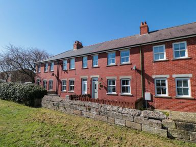 A row of red brick terraced houses with white framed windows and small front yards at The Tannery in Whitby
