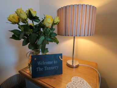A wooden table with a vase of yellow roses a table lamp and a welcome sign at The Tannery in Whitby