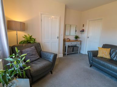 A room with two leather chairs a table lamp a wooden side table with mirror and two white doors at The Tannery in Whitby
