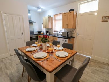 A kitchen with wooden cabinets a dining table set for six with plates glasses and flowers at The Tannery in Whitby