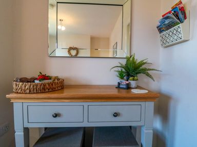 A wooden table with two drawers holding a basket with strawberries a plant a card holder and a wall mirror above at The Tannery in Whitby