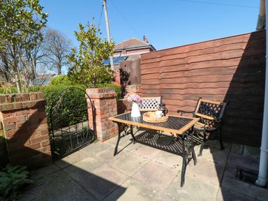 A small outdoor patio with a table, two chairs, a brick wall, and a metal gate at The Tannery in Whitby