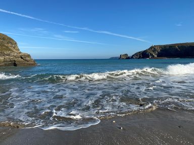 A beach with waves crashing on the shore and rocky cliffs in the background at The Chace in Portreath