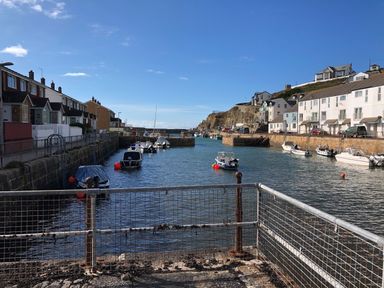 A small harbor with boats docked along stone walls and houses lining both sides at The Chace in Portreath