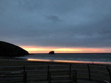 A beach at sunset with a rock formation in the sea and benches overlooking the shore at The Chace in Portreath