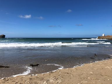 A sandy beach with waves and a stone pier with a white structure at The Chace in Portreath