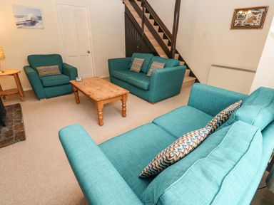 A living room with teal sofas a wooden coffee table stairs and paintings on walls at The Chace in Portreath