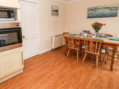 A dining area with a wooden table set with plates and glasses next to a built-in oven and microwave at The Chace in Portreath